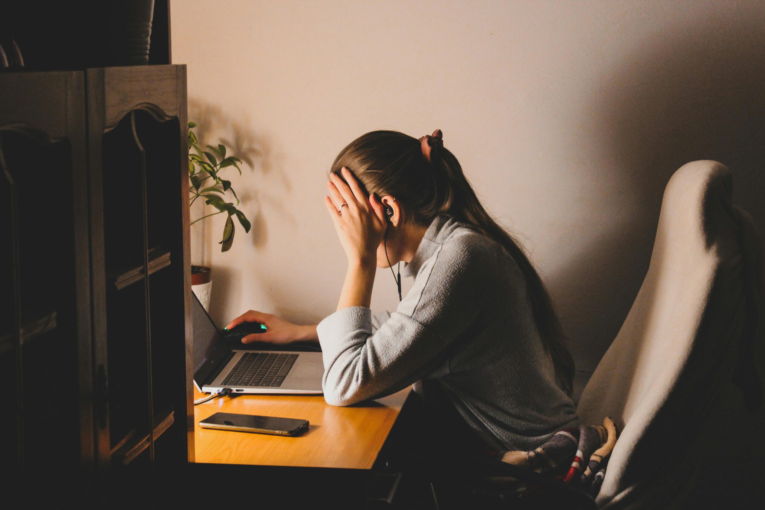 A young woman using a laptop at home, stressed, in casual attire.