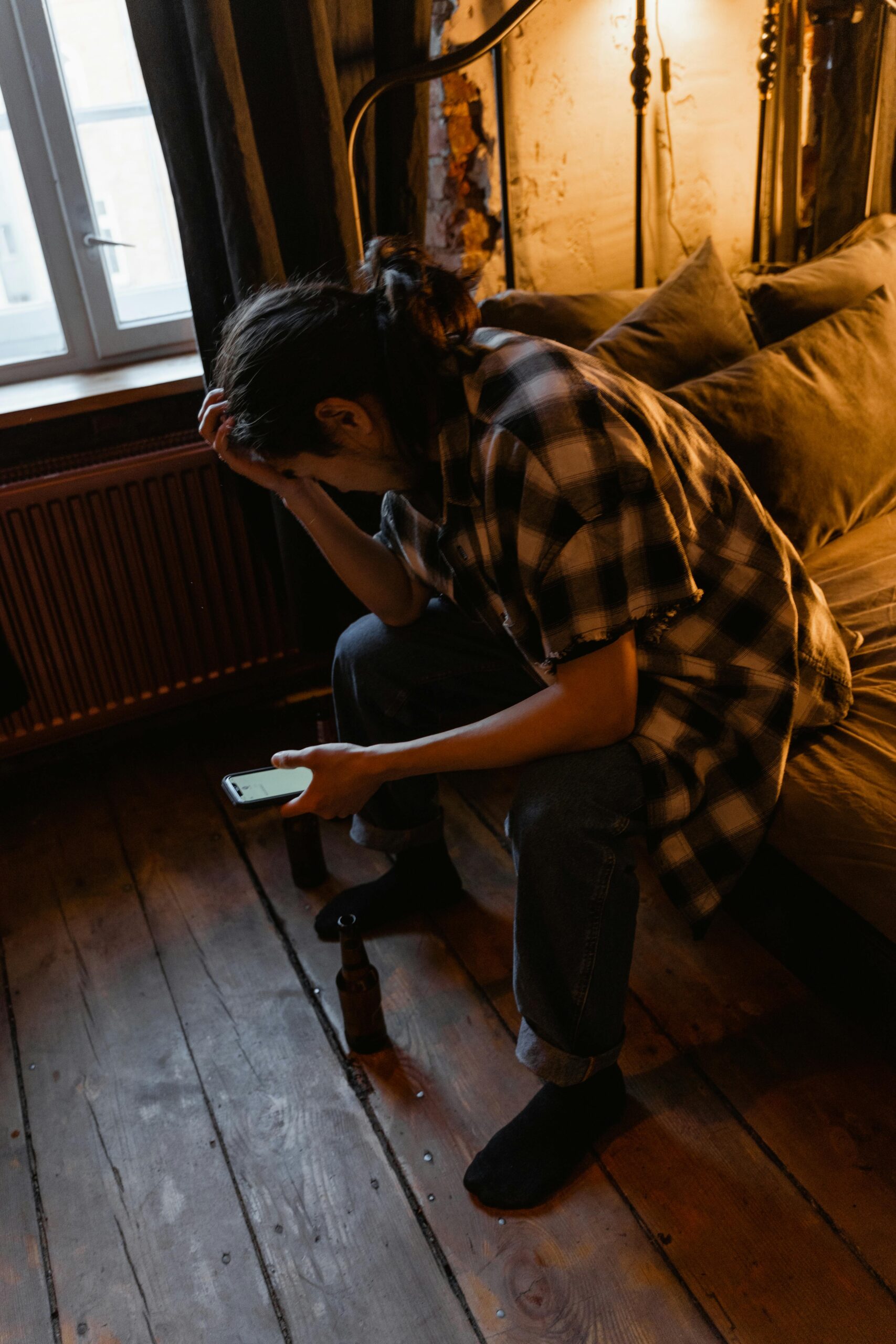 A young adult sits indoors, looking contemplative and holding a phone, creating a thoughtful mood.